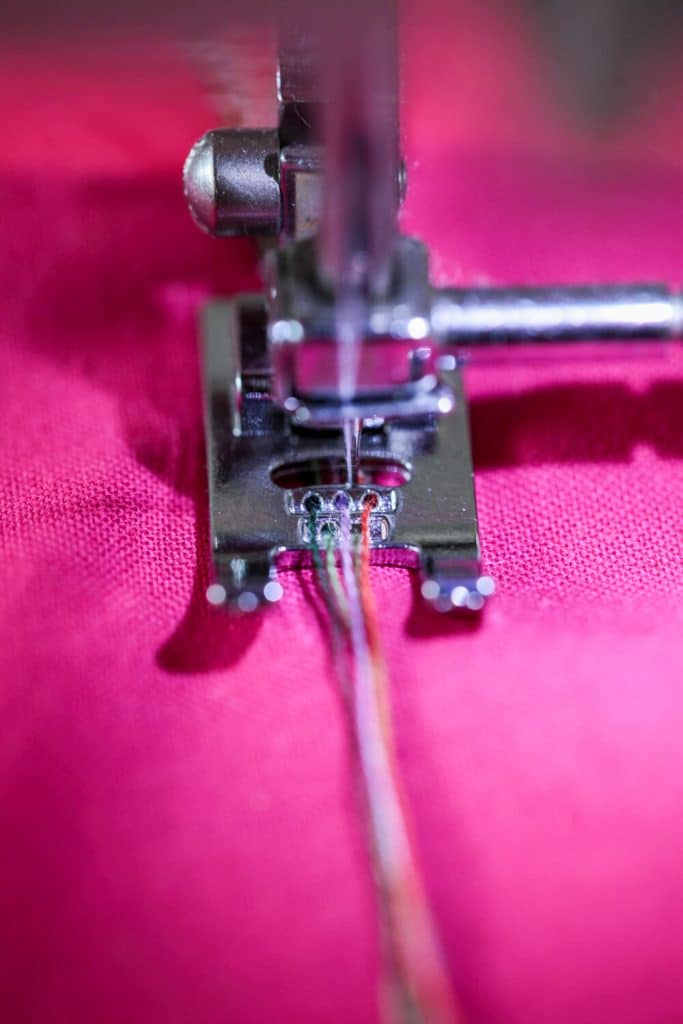 Les 5 ou 7 cordons de fil à broder sont insérés dans le pied presseur, avant d'être cousus au point zig zag triple